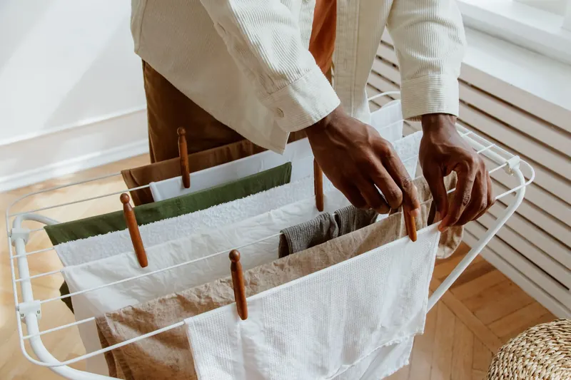 A close-up of a person hanging laundry on an indoor drying rack, highlighting domestic life