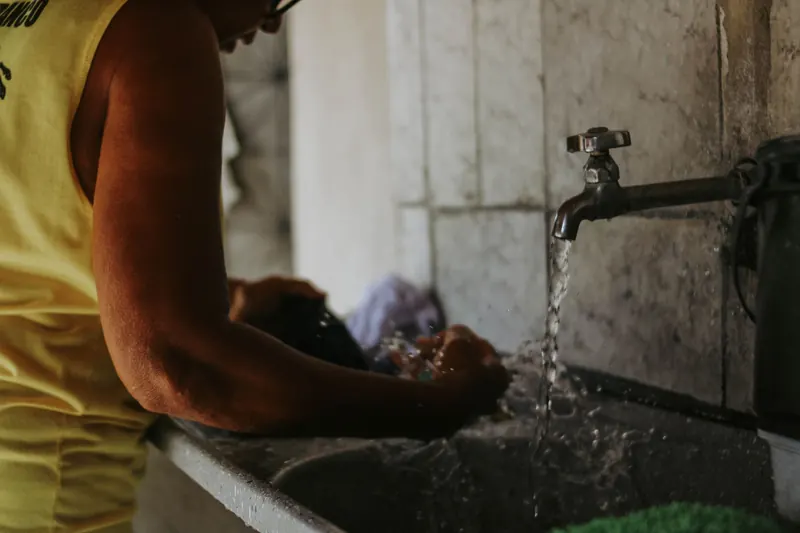Close-up of a person washing clothes in a sink with running water indoors
