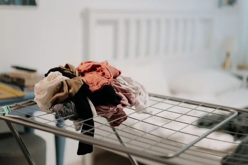 Pile of clothes on a drying rack in a cozy bedroom setting with natural light