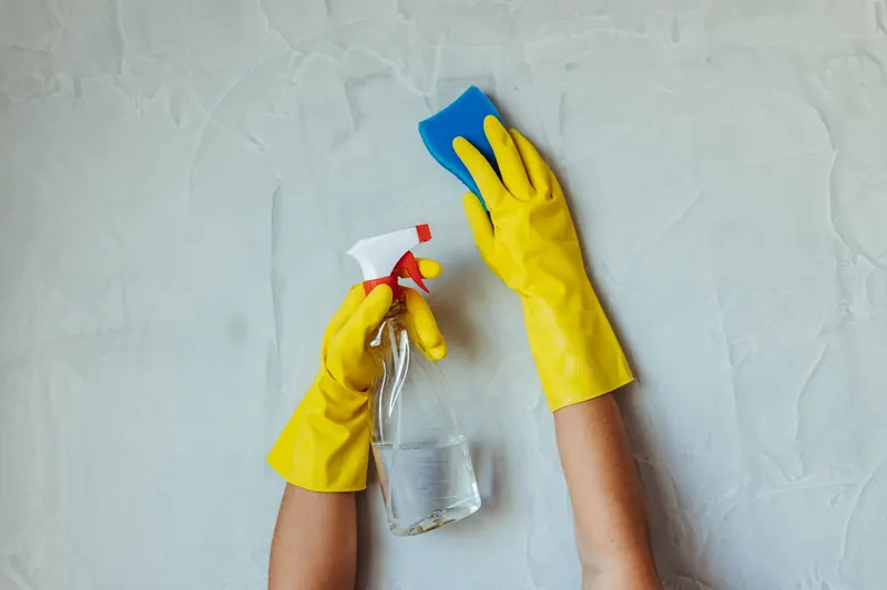 Close-up of hands in yellow gloves cleaning a wall with a spray bottle and sponge