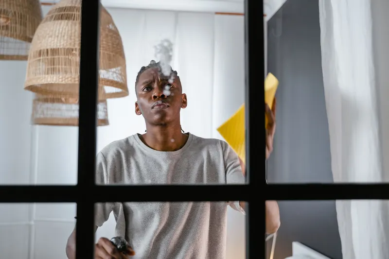 Man using a spray bottle and cloth to clean a glass window indoors
