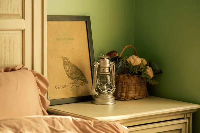 Warmly lit bedroom corner with poster, lantern, and floral basket adding vintage charm