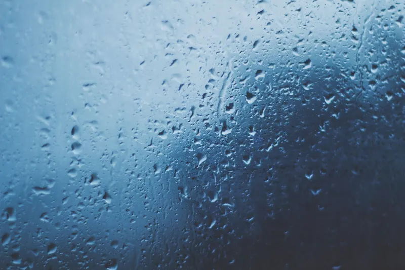 Detailed view of water droplets on a glass window with a blue background